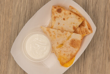 Overhead view of hearty appetizer of quesadilla wedges with melted cheese and sour cream as a...