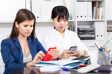 Obraz premium Two women write sms by phone in the office