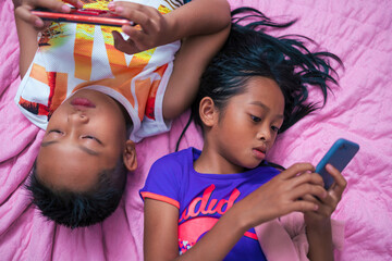 Fototapeta premium Asian girls and boys using smart phones on their bed at home during the day.
