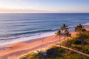 Aerial view over Gold Coast beach and ocean with palm trees and sunrise light.
