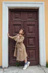 Young millennial woman with wild hair dressed in an autumn coat posing near the door of an old building.