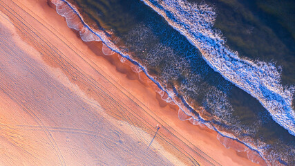 Aerial view over beach and ocean with sunrise light.