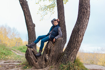 Tall handsome man climbing on the tree in autumn forest