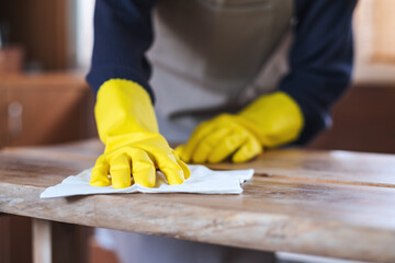 Closeup image of a housewife wearing protective glove, cleaning and washing wooden table at home