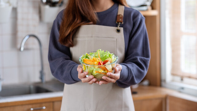 Closeup image of a woman holding and showing a fresh mixed vegetables salad in the kitchen at home