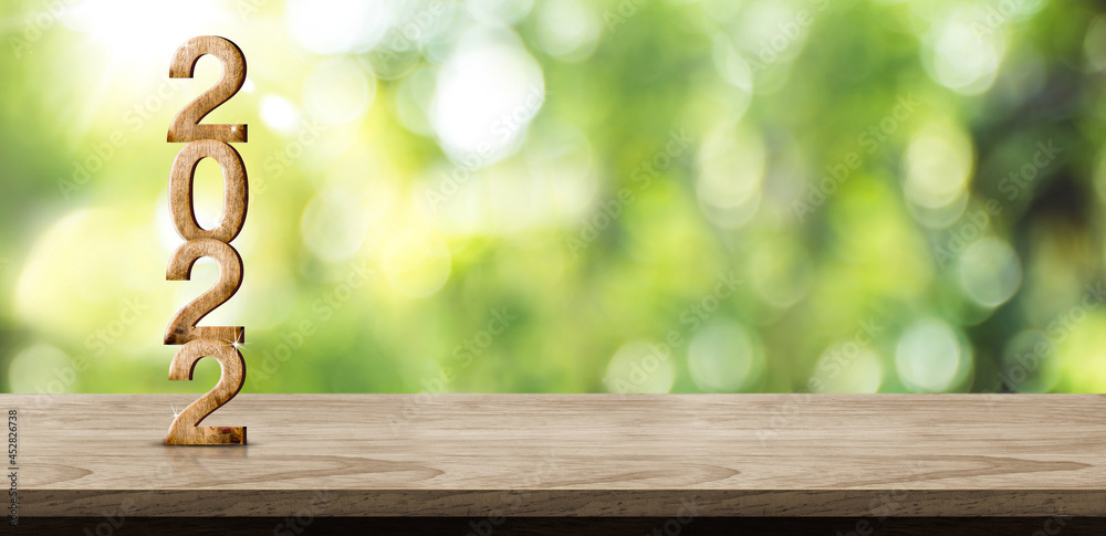 Aufkleber New year 2022 wood number (3d rendering) on wooden table at blur abstract green tree garden bokeh background,Mock up banner space for display of product or design.Ecology holiday backdrop