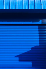 Sunlight and shadow on surface of automatic blue roller shutter door with steel awning in vertical frame