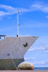 Cargo ship moored at port against white clouds on blue sky background in vertical frame