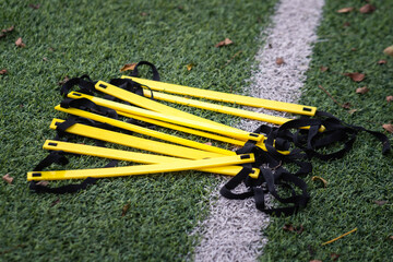 A speed and agility ladder, football training gear, which is placed on soccer turf pitch. Sport training equipment object photo. Selective focus at the equipment part.