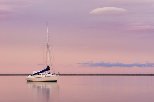 A sailboat at sunset reflects in calm water in Motueka, Tasman Bay, New Zealand