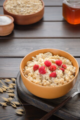 A bowl of oatmeal porridge with raspberries, strawberries and honey next to ear of oats lying on the table. Healthy breakfast. Vegan and vegetarian food.