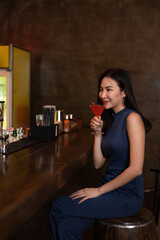 Nightlife concept a gorgeous girl in a blue collared dress looking confident sitting beside the bar sipping the pink cocktail