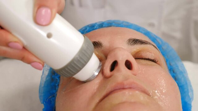 Modern beauty clinic with hardware cosmetology. Middle aged woman getting rf lifting skincare facial procedure. skin rejuvenation. Mature client getting face rf-lifting treatment. 4 k video