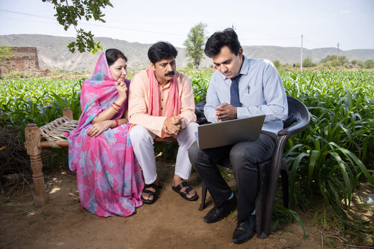 Happy rural indian farmer family with agronomist or banker use laptop. Man officer showing policy on computer screen, Financial support or farming crop loan, husband wife with government scheme agent