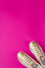 Pair of golden female sneakers on pink background