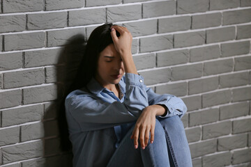 Depressed young woman sitting near brick wall