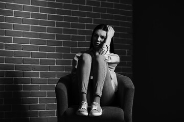 Black and white portrait of depressed young woman sitting near brick wall