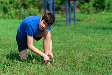 teenage boy exercising outdoors, sports ground in the yard, he ties his shoelaces and does a warm-up, healthy lifestyle