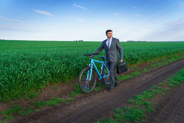 Obraz premium Businessman with a bicycle posing in a green grass field - business concept for freedom, vacation or freelance. Beautiful spring nature.