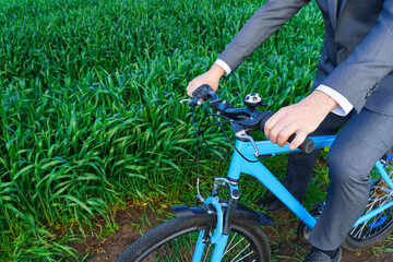 Obraz premium Businessman's hand with a bicycle posing in a green grass field - business concept for freedom, vacation or freelance. Beautiful spring nature.