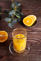 Fresh orange glass of juice with ice and oranges on rustic wood background.