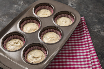 Baking tin with uncooked poppy seed muffins on dark background
