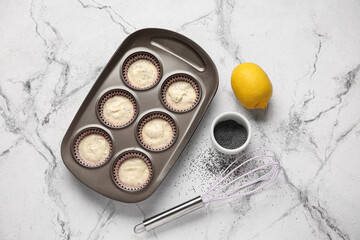 Baking tin with uncooked poppy seed muffins on light background