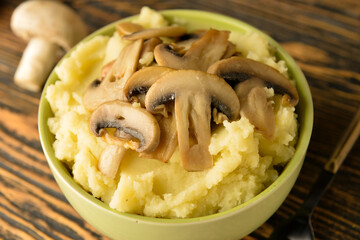 Bowl with tasty mashed potatoes and mushrooms on wooden background, closeup