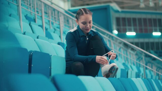 Young girl is lacing up her skates while sitting on the bleachers