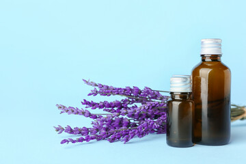 Bottles of lavender essential oil and flowers on color background
