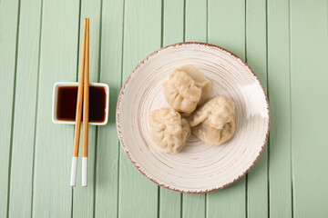 Plate with tasty dumplings, chopsticks and bowl of sauce on color wooden background