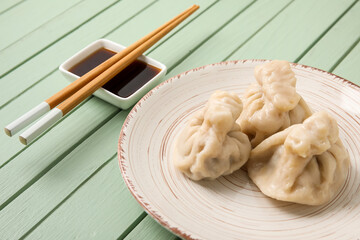 Plate with tasty dumplings, chopsticks and bowl of sauce on color wooden background, closeup