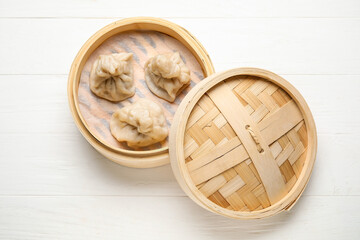 Bamboo steamer with tasty dumplings on light wooden background
