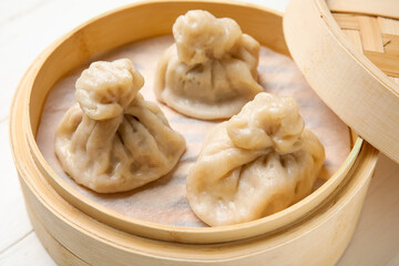Bamboo steamer with tasty dumplings on light wooden background, closeup