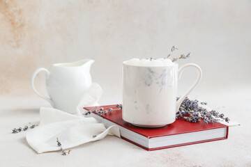 Cup of tasty lavender latte, book and flowers on light background