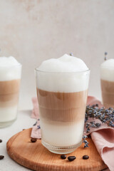 Glasses of tasty lavender latte, coffee beans and flowers on light background