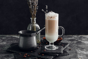 Glass of tasty lavender latte, coffee pot and flowers on dark background