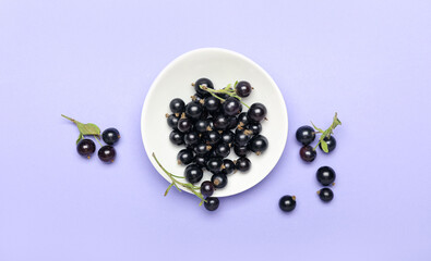 Plate with ripe black currant on color background