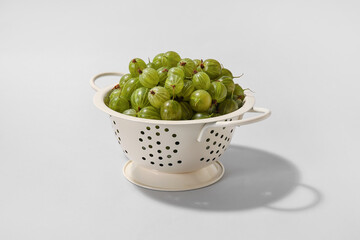 Colander with fresh ripe gooseberry on light background