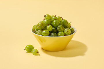 Bowl with fresh ripe gooseberry on color background