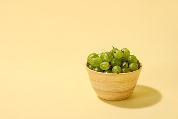 Bowl with fresh ripe gooseberry on color background