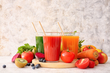 Glasses with healthy juice, fruits and vegetables on light background