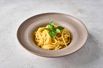 Spaghetti pasta and basil on ceramic plate on light background. Close up