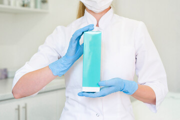 Doctor woman holding a blue box with medicine or cosmetics, an empty box without labels on the background of a doctor's office. Concept layout for advertising of medical drugs.