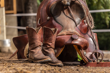 Ranch life scenery: muddy western boots in front of a western saddle. Cowboy boots. Muddy working...