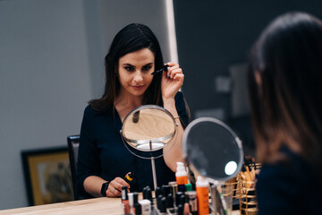 Fototapeta na wymiar Young beautiful woman making make-up near mirror