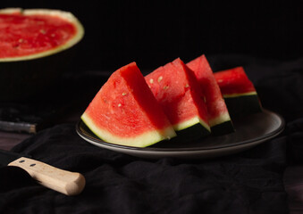 Pieces of watermelon on a black background and a knife. Rustic style.
