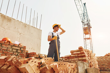 Tired man. Young construction worker in uniform is busy at the unfinished building