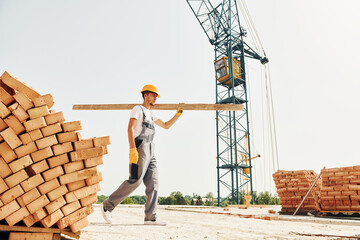 With wooden plank. Young construction worker in uniform is busy at the unfinished building