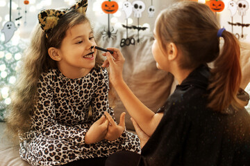 halloween, holiday and childhood concept - smiling little girls in party costumes doing face...